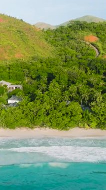 Turkuaz suların yavaşça kumlu kıyıya yuvarlandığı yemyeşil bitki örtüsüyle kaplı tropikal bir sahil. Anse Lazio, Seyşeller.