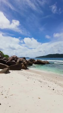 Granit kayalar, berrak bir gökyüzünün altında yemyeşil yemyeşil ile çevrili turkuaz bir plajın kıyıları boyunca uzanır. Seyşeller, Praslin.