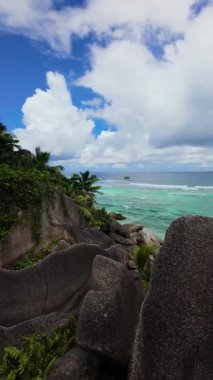 Bereketli yeşilliklerle çevrili granit kayalar bulutlu gökyüzünün altındaki turkuaz okyanus sularını gözden kaçırıyor. Seyşeller, La Digue.