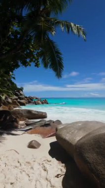 Büyük granit kayalar turkuaz dalgaların yanında beyaz kumlu bir plaja gölge düşürür. Seyşeller, Praslin. Anse Georgette.