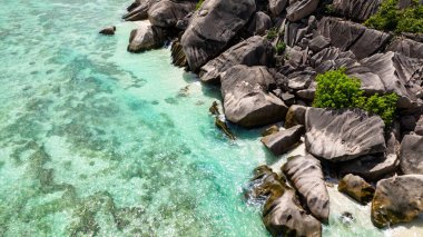 Turkuaz deniz yavaşça süzülürken, beyaz sahilde dinlenen granit kayalar. Seyşeller, La Digue.
