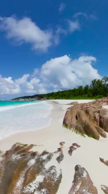 Parlak mavi gökyüzünün altında pürüzsüz granit kayalar ve turkuaz okyanusla beyaz kumsal. Seyşeller, La Digue. Küçük Anse.