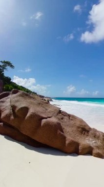 Plajda granit kayalar ve mavi gökyüzünün altında turkuaz okyanus dalgaları. Seyşeller, La Digue. Küçük Anse.