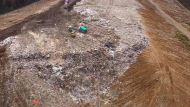 Çalışan çöp kamyonları olan büyük bir çöp yığını, manzaralı. Ev atıkları. Ormandaki çöplük, üst manzara..