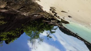 Turkuaz sular mavi gökyüzünün altında yoğun tropikal yeşillikle kayalık bir kıyı şeridine çarpar. Seyşeller, Mahe.