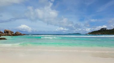 Turkuaz dalgalar yavaşça sahile çarpıyor ve kumların üzerinde dallar uzanıyor. Anse Cocos. Seyşeller, La Digue.