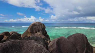 Turkuaz bir okyanusa bakan granit kayalar mavi gökyüzü ve dağınık bulutlar. Seyşeller, La Digue.