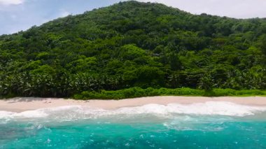 Turkuaz suları, beyaz kumu ve arka planda yoğun yeşil tepeleri olan sakin bir sahil. Seyşeller, Mahe.