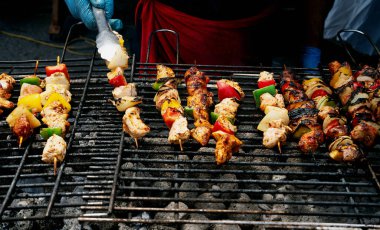 Eldivenli biri, salamura edilmiş et ve sebze şişlerini kızgın ızgarada pişiriyor ve dumanı yükseliyor..