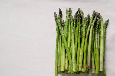 Tarafsız kumaş arka planında taze yeşil kuşkonmaz sapı. Kuşkonmaz mızrakları düzgün bir demet halinde sergileniyor, uçlarını ve canlı yeşil renklerini sergiliyorlar..