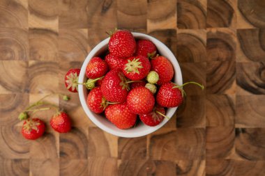 Tahta kesme tahtasındaki kasedeki taze çilekler. Doğal ve organik sunumları vurgulayarak kasenin yanına saçılmış çilekler..