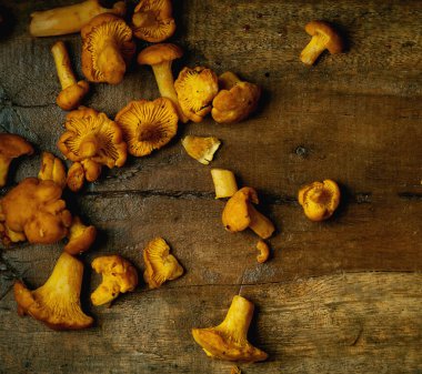 Kırsal ahşap zemine serpilmiş taze chanterelle mantarları. Zengin altın tonlar organik dokuyu vurgular. Az aydınlık estetik. Kırsal mutfak teması için genel görünüm.