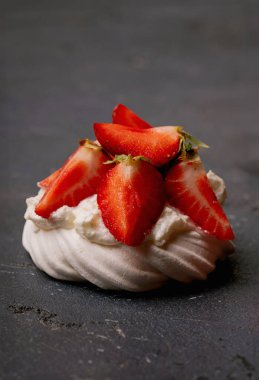 Üzerinde dilimlenmiş çilek ve koyu dokulu arkaplan olan bir kremanın yakın çekimi. Canlı kırmızı çilekler beyaz krema ve narin kremayla tezat oluşturuyor. Minimalist sunum.