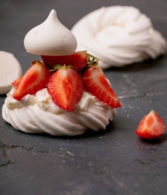 Üzerinde dilimlenmiş çilek ve koyu dokulu arkaplan olan bir kremanın yakın çekimi. Canlı kırmızı çilekler beyaz krema ve narin kremayla tezat oluşturuyor. Minimalist sunum.