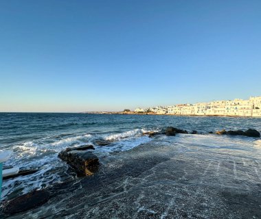  Naousa, Paros, Ege Denizi kıyı manzarası. Kristal berrak su, yumuşak dalgalar, beyaz Kiklad binalar, sakin günbatımı ışığı, sahil köyü.