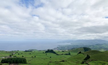 Azores Adası Sao Miguel manzarası. Yuvarlanan yeşil tepeler, yoğun ormanlar, bulutlu gökyüzünün altında volkanik göl manzarası. Doğayla, dağlarla ve canlı bitkilerle büyüleyici manzara ufku.