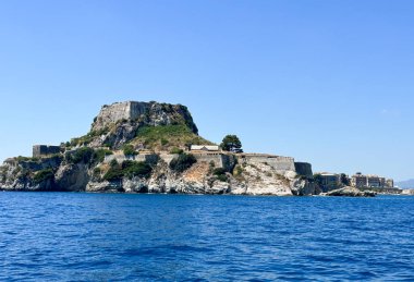 Yunanistan 'ın Korfu Adası' ndaki Corfu Kalesi kıyı manzarası. Mavi İyon Denizi ile çevrili kayalık tepenin üzerindeki antik taş kale. Temiz gökyüzü, tarihi mimari ve yemyeşil..