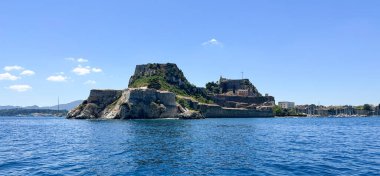 Yunanistan 'ın Korfu Adası' ndaki Corfu Kalesi kıyı manzarası. Mavi İyon Denizi ile çevrili kayalık tepenin üzerindeki antik taş kale. Temiz gökyüzü, tarihi mimari ve yemyeşil..