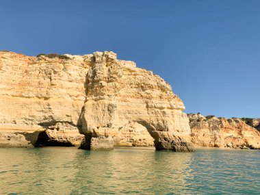 Algarve 'ın doğal kaya oluşumları ve turkuaz suları olan kıyıları berrak mavi gökyüzünün altında, bir tekneden. Canlı dokular ve dingin okyanus manzaraları Portekiz 'in kıyı şeridinin güzelliğini yansıtıyor.