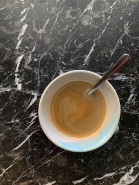 Mermer bir masada köpüklü bir fincan espresso, fincanın yanında duran bir kaşık..