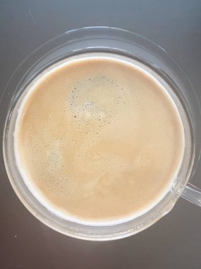 Top view of a frothy coffee in a transparent glass cup placed on a dark surface. Smooth crema texture visible, minimalistic composition, clean and simple presentation. clipart