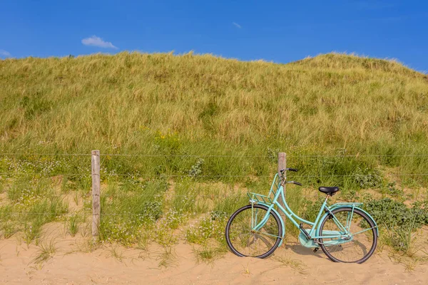 A blue bicycle against the fence in the Dutch dunes