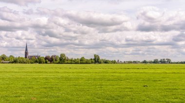 Beautiful Dutch polder landscape with cloudy sky, green meadow and a church in the background