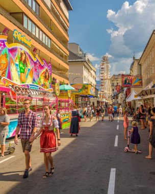 Villach, Austria - August 5, 2022: People in traditional costumes visit the Villach Kirchtag with fairground in the background