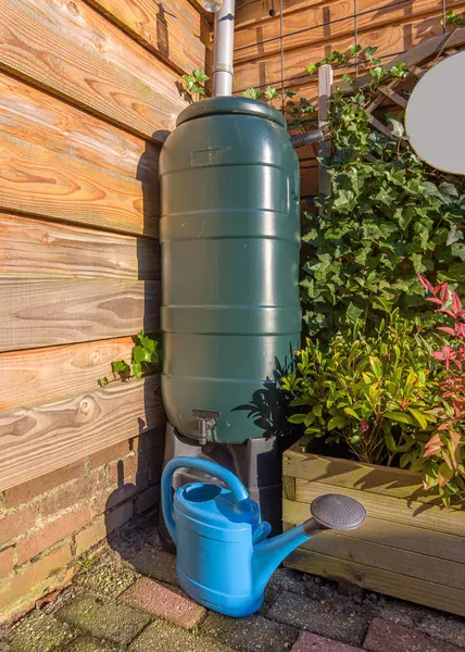 在花园里的一个蓝色水壶的绿色雨桶 图库图片