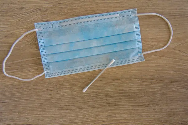 A medical face mask with a cotton swab on a wooden background