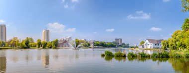 Gent, Belçika 'daki Watersportbaan panoramik manzarası sakin su, modern apartman binaları ve açık mavi gökyüzü altında yeşil çevreyi gösteriyor.