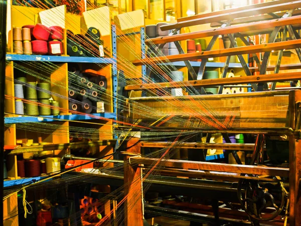 Colourful weaving in factory with green and orange cotton strands leading to loom