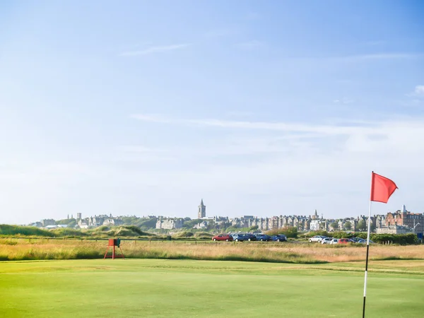 Red hole flag on golf course with urban skyline behind at St Andrews Scotland.