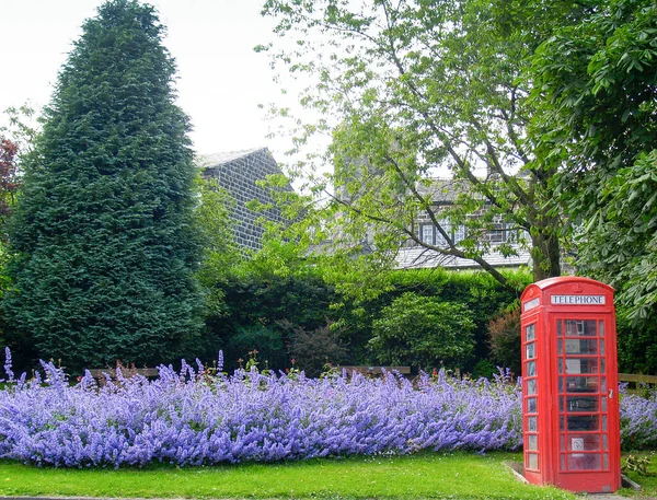 ヘプトンストール英国 2009年6月29日郊外の通りで明るい青の花に裏打ちされた英国の赤い電話ブース — ストック写真