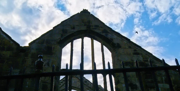 Old stone gable structure in silhouette against blue sky with white clouds at Heptonstall, United Kingdom.