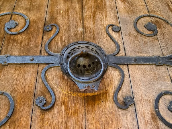 Black wrought iron antique door pull on old wooden plank door closeup.