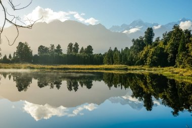 Mathieson Gölü 'ndeki yansımalar, Yeni Zelanda' nın güneyindeki doğal çalı, orman ve Güney Alpler sıradağlarıyla çevrilidir..