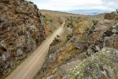 Dirt track through rock cutting on Central Otago Rail Trail in South Island New Zealand. clipart