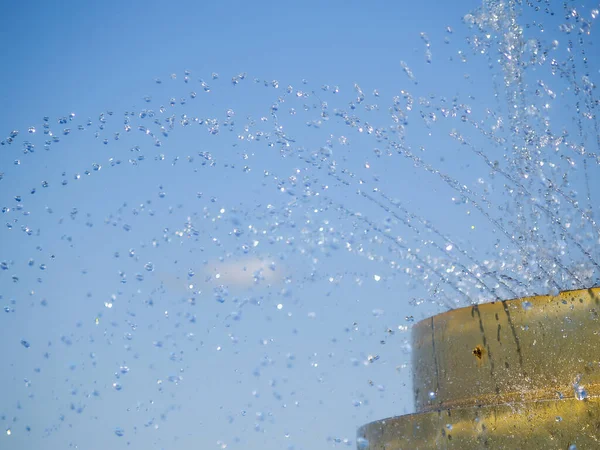 Water spray and droplets from fountain against blue sky.