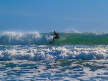 Güneş doğarken mavi gökyüzünün altında dalgaların içinde siluet içinde sörfçü..