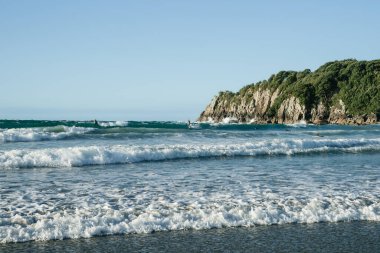 Multiple Surf waves roll in onto Main Beach, Mount Maunganui by Moturiki Island  on summer day.