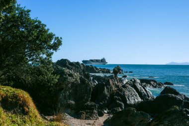 Small container ship passing rocky base Mount Maunganui entering Port of Tauranga.