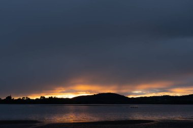 Dramatic deep cloudy sky in sunrise landscape over Tauranga harbour.