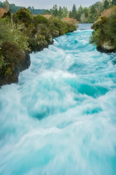 Long exposure moving water of Huka Falls rapid water surging through bush clad gorge at Taupo New Zealand.
