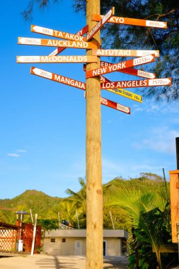 Tall sign post pointing directions to cities and towns around Cook Islands and world near beach in Rarotonga in Cook Islands.