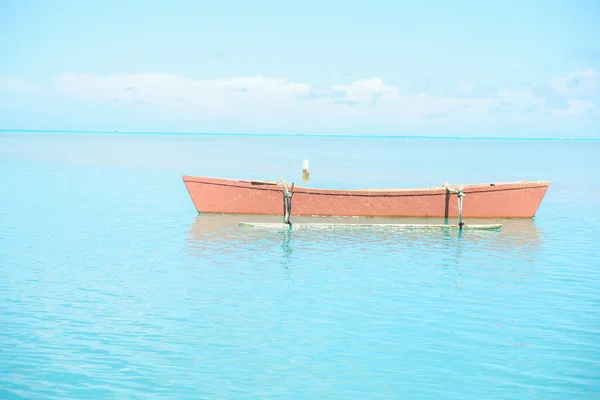 Orange color outrigger canoe on turquoise tropical water view to heat shimmer effect on distant horizon.