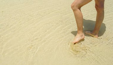 Legs standing in coral sand and shallow water on reef in tropical lagoon.