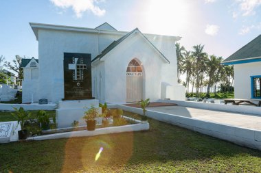 Aitutaki Cook Adaları - 8 Kasım 2010; Ziona tapu yoluna çıkan yol, arkasında güneş ve mercek efekti olan kapalı kapılı beyaz kilise tabelası.