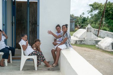 Aitutaki Cook Adaları - 9 Kasım 2010; Ada çocukları kilisenin dışında mutlu bir şekilde oturup gülümsüyor ve el sallıyorlar..