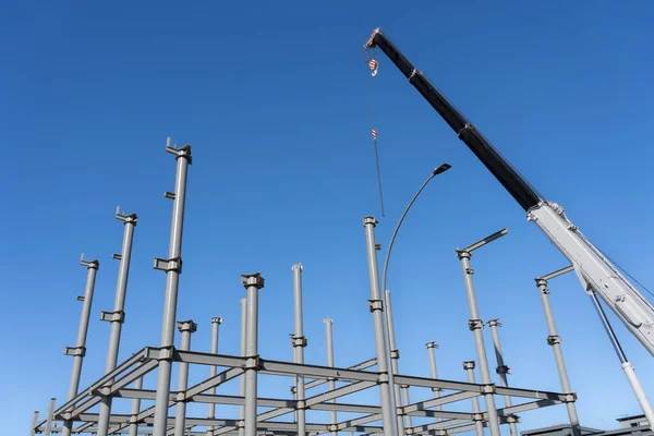 青い空の下で新しい建物のための構造鋼フレーミング上に高くそびえる建設クレーン — ストック写真